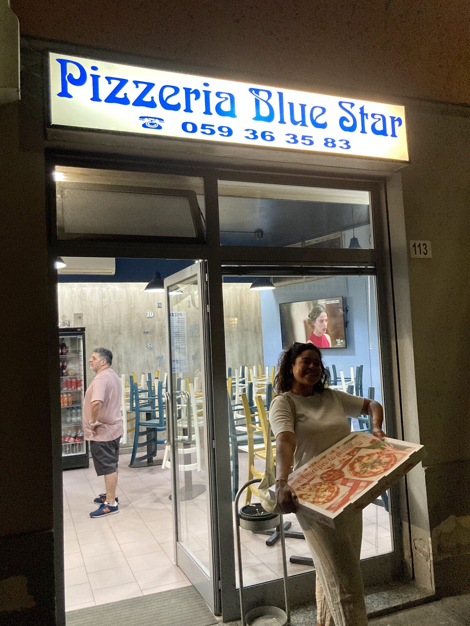 L'insegna blu della Pizzeria Blue Star a Modena, la sera, con una pizza appena sfornata